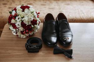 A man's shoes and belt are displayed on a table next to a bouquet of flowers photo