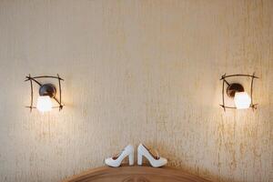 Two white shoes are on a table in front of a wall with two light fixtures photo