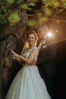 A bride and groom are posing for a picture in front of a tree photo