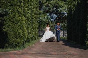 A bride and groom walk down a path in a park photo