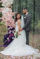 A bride and groom are posing for a picture in front of a pink arch photo