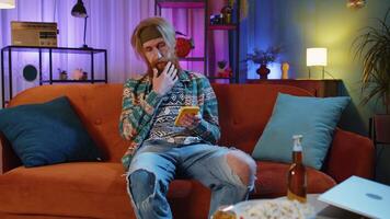 Portrait of hippie man sitting on sofa, using smartphone share messages on social media application video