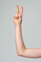Close-Up of a Persons Arm Showing a Peace Sign Against a Grey Background photo