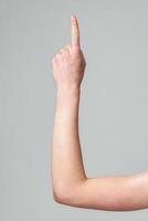 Close-Up of a Human Arm Raised and Pointing Upwards Against a Gray Background photo
