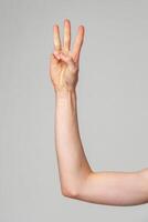 Hand Gesturing Number Three Against a Plain Background in Natural Light photo