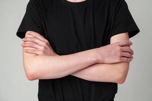 Close-Up View of a Person Standing With Arms Crossed in a Black T-Shirt Against a Grey Background photo