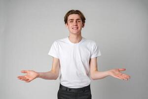 Young Man in White T-Shirt Gesturing With Open Arms Against a Plain Background photo