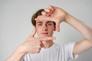 Young Man Making Frame With Hands Focusing On an Imaginary Object Against a Plain Background photo