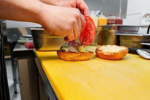 Chef Adds Sliced Tomato to a Gourmet Burger on a Busy Kitchen Countertop photo