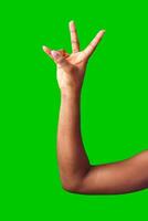 A hand making a gesture with a green background during daylight photo