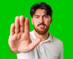 Man with a beard holding up his hand and looking at the camera against a bright green background photo