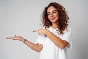 A young woman with curly hair playfully pointing finger while standing against a gray background photo