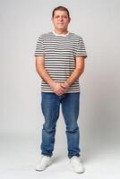 A man stands confidently in a striped shirt, casual jeans with a neutral background photo