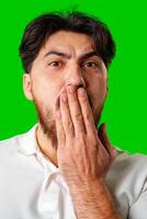 A man with a surprised expression holds his face while against a vibrant green background photo