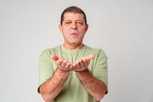 Elderly man demonstrating an open-handed gesture while standing against a plain background photo