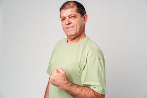 Confident older man posing with a clenched fist in a light green shirt against a neutral background photo