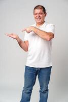 Man dressed in a white polo shirt and jeans happily pointing to the side against a plain background photo