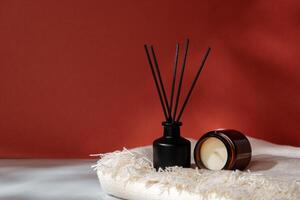 Aromatic Reed Diffuser and Scented Candle on a Woven Mat Against a Warm Red Background photo