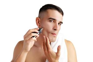 Handsome young man shaving face with electric razor on white background photo