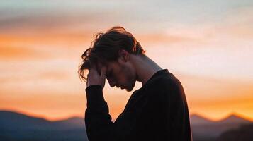 Silhouette of a young man contemplating at sunset against a backdrop of mountains in the evening sky photo