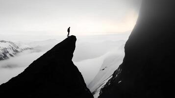 A lone hiker stands on a rocky outcrop overlooking a breathtaking snowy mountain landscape during twilight photo