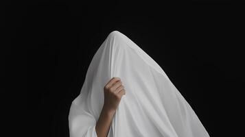 A person partially concealed by a flowing white cloth against a black background, creating an enigmatic and surreal appearance photo
