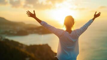 A woman stands with arms outstretched toward a vibrant sunset over the ocean, celebrating the beauty of nature from a scenic viewpoint photo