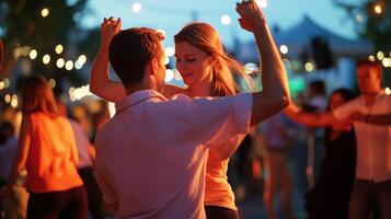 Couple dancing joyfully at an outdoor twilight festival with string lights, surrounded by friends and vibrant atmosphere photo