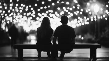 Couple sitting on a bench under twinkling lights at night, enjoying a romantic moment in a lively park filled with soft illuminations photo