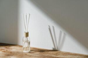 Sunlit Diffuser Bottle With Reeds Casting Shadows on a White Wall photo