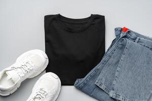 T-shirt, jeans and white sneakers on gray background top view photo