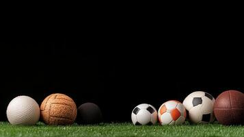 A collection of various sports balls arranged neatly on green grass against a dark background photo