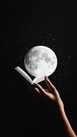 A hand holding an open book releases a large full moon under a starry night sky photo