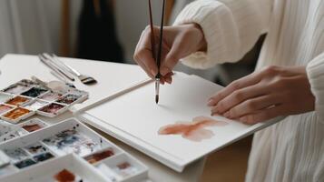 A person creates a watercolor painting at a bright indoor workspace with art supplies on a table during the daytime photo