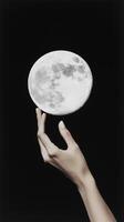 A hand gently reaches towards a glowing full moon against a dark background, creating a surreal and dreamlike atmosphere photo
