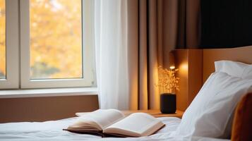 A cozy bedroom corner with an open book, morning sunlight filtering through sheer curtains, and autumn leaves visible outside photo