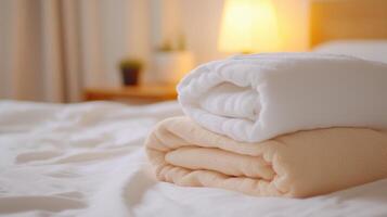 Soft white and beige towels neatly stacked on a cozy bed in a warmly lit room with a bedside lamp in the background photo