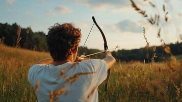 A young archer practicing with a bow at sunset in a grassy field surrounded by trees photo