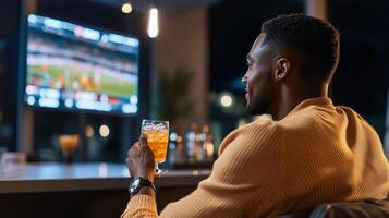 A man enjoys a drink while watching a sports game on a large screen in a modern lounge during the evening photo