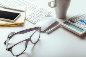 Office desk table with computer keyboard, supplies, calculator, pen, glasses photo