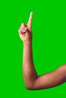 A hand making a gesture with a green background during daylight photo