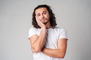 A young man stands thoughtfully against a plain background, expressing contemplation photo