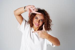A woman in a white shirt and ripped jeans posing positively with a playful expression in a light studio setting photo