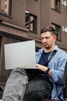 Young man working on a laptop while seated on a bench outside photo