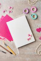 A collection of crafting materials arranged on a textured surface with a blank notebook, decorative paper, and various embellishments photo