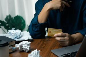 Man Holding Credit Card While Using Laptop at Desk with Crumpled Paper online shopping or financial transactions. photo