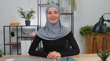 Businesswoman working smiling friendly at camera and gesturing hello assalamu alaikum at home office video