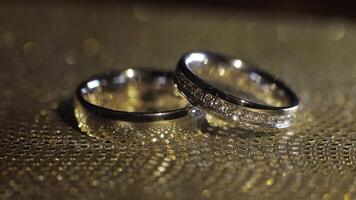 Wedding rings lying, rotate, spinning on shiny golden shining surface with light, close-up macro video