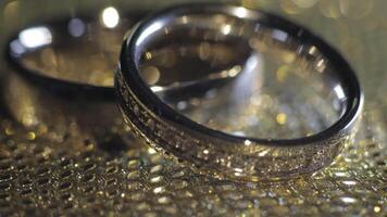 Wedding rings lying, rotate, spinning on shiny golden shining surface with light, close-up macro video