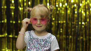 Child smiling, pointing fingers at camera. Girl posing on background with foil golden curtain video